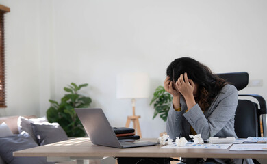 Tired business woman in stress works at a laptop while sitting at a table at home and holds her hand on her temples, migraine attack. Freelance, work from home.