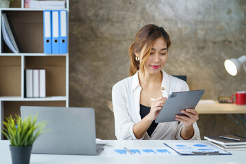 Wall Mural - Bright and beautiful young Asian business woman happily at the office to come up with new ideas to work using a tablet smiling.