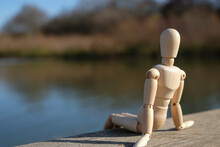 A Wooden Mannequin Doll Sits On A River Bridge. Copy Space.