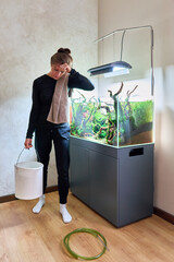 Poster - A woman holds heavy white bucket full of water in front of the aquarium aquascape. Strong woman and water changing concept.