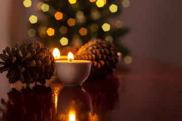 Decoração de Natal. Algumas velas acesas em uma superfície reflexiva, duas pinhas e um detalhe desfocado da árvore de Natal ao fundo.