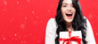 © Tierney - Happy young woman holding a Christmas gift box on a red background