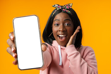 Portrait of a excited young african woman showing blank screen mobile phone over yellow background