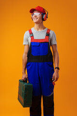 Wall Mural - Portrait of young foreman worker with toolbox over yellow background