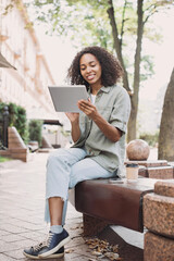 Wall Mural - Smiling young woman  using digital tablet in a city. Beautiful student girl having coffee break. Modern lifestyle, connection, business, freelance work concept