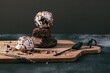 Ice cream ball over two pieces of chocolate cake in small plate on wooden board with spoon