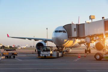 Wall Mural - Aircraft is attached to the terminal gangway of the airport building preparation for towing and launch flight in the evening at sunset.