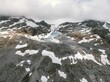 Aerial shot of gray rocky mountains and highlands with some snow, and clouds in the background
