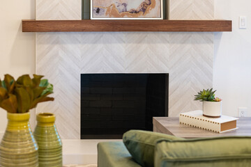 Modern fireplace view over couch of patterned tile facing, wood bean mantle, and green accents decor.