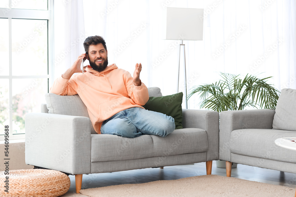 Handsome bearded man talking by tablet computer on grey sofa at home