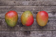 Mango fruits on wooden background. Top view. Three ripe mangoes laid in row on dark wooden board. Photo directly from above.