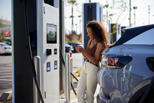 Young Woman Text Messaging At Electric Vehicle Charging Station
