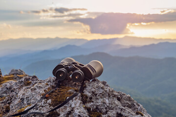 binoculars on top of rock mountain at beautiful sunset background.