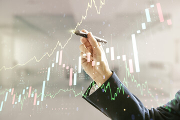 Wall Mural - Man hand with pen working with abstract virtual financial graph on blurred office background, forex and investment concept. Multiexposure