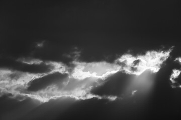 Wall Mural - Black and white cloudscape background of sun rays beaming through dramatic monsoon clouds in the sky.