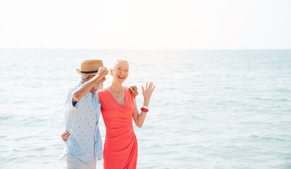 Happy senior couple using smart phone together on the beach having fun in a sunny day, activity after retirement in vacations and summer.