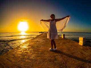 Wall Mural - Woman walking on pier near sunny, tropical beach at daybreak
