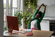 © DimaBerlin - Tired African woman freelancer doing stretching exercises, working remotely on computer in kitchen at home. Black girl taking break from freelance work or online study, relaxing at remote workplace