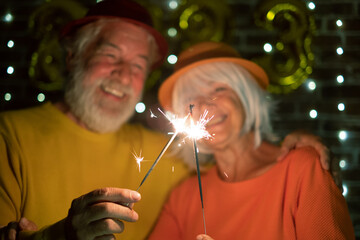 Wall Mural - Blurred caucasian senior couple holding sparklers celebrating new year. Happy lifestyle for mature retirees, party lights