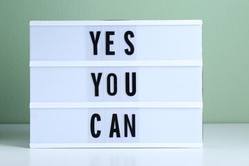 Wall Mural - Lightbox with phrase Yes You Can on table against light green background. Motivational quote