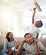 © David L/peopleimages.com - Happy family playing living room with toy airplane for fun games, freedom and energy together in family home. Parents, kids and flying aeroplane toys to dream for travel, easy lifestyle and happiness
