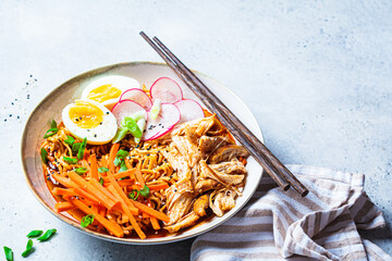 Wall Mural - Chicken ramen bowl with carrots, noodles, egg, radish and green onions, gray background.