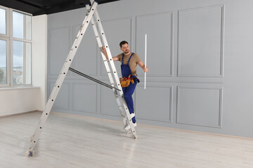 Poster - Electrician in uniform with ceiling lamp on metal ladder indoors