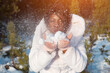 happy dark-skinned girl blows on frosty snow pile in hands falling and sparkling under bright sun rays closeup