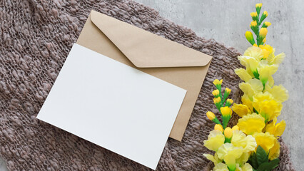 Flat lay shot of white blank card and eco paper envelope on yarn  background with flower