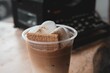 Closeup of a latte coffee in a plastic cup topped with marshmallows and crackers