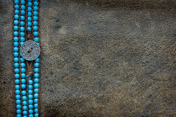 Wall Mural - brown leather background with a frame of turquoise beads with a metal button close-up