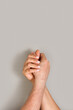 © Mercedes Fittipaldi - Mano de mujer y de hombre unidas y entrelazadas sobre un fondo gris. Vista de frente y de cerca. Copy space. Formato vertical