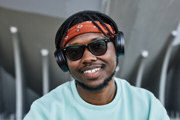 Wall Mural - Portrait of young black man wearing headphones looking at camera outdoors and smiling