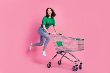 Wall Mural - full body photo of carefree overjoyed lady jumping push supermarket trolley isolated on pink color b