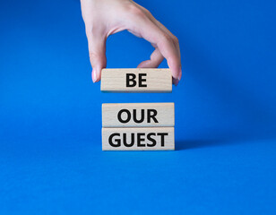 Be our guest symbol. Concept word Be our guest on wooden blocks. Businessman hand. Beautiful blue background. Business and Be our guest concept. Copy space