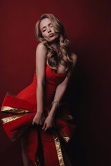 Wall Mural - beautiful woman with blond hair in elegant red dress holding a big red bow, posing in the studio