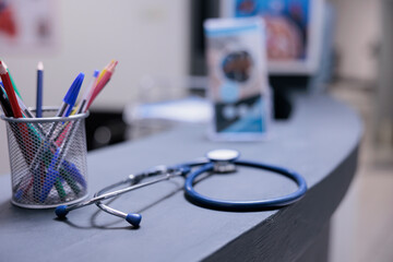 Medical equipment on front desk top with pens and information leaflets in hospital reception. Stethoscope on table in clinic administrative area. No one using medical equipment to check patients.