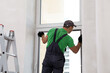 Worker in uniform installing double glazing window indoors, back view