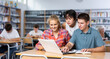 © JackF - Smiling teenage boy and girls using laptop at college library, watching videos