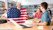 © JackF - Group of teenagers listening to aged female teacher holding USA flag at Geography lesson in school library
