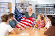 © JackF - Mature woman teacher conducting a extracurricular lesson in the school library tells the schoolchildren the history of USA and shows the national flag