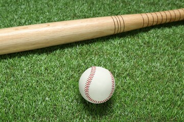 Wooden baseball bat and ball on green grass. Sports equipment