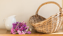 Brown Wicker Basket In Bright Sunlight On Shelf Wth Purple Daisies And White Jug In Background (selective Focus)