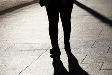 Black Silhouette And Shadow Of Overweight Woman Walking On A Street. Female Legs On Paved City Sidewalk