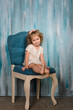 girl in light clothes sits on an old vintage chair, against a blue wall