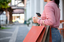 Woman Carrying Her Shopping Bags And Using Her Smartphone While Shopping At The City Square.