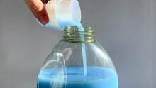 A stream of blue liquid laundry detergent is poured from a plastic measuring cap to bottle. 
