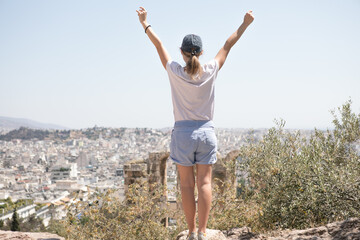 The girl at sunset. The girl stands with her back on the top of the mountain and looks at the sunset, welcomes the sun with her hands up Athens in Greece.