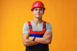 Young construction worker in helmet and uniform posing on yellow background in studio