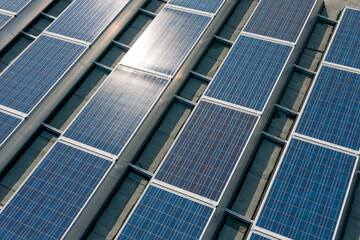 Drone view on a large array of solar panels on a roof in the warm summer light under a blue sky producing electrical power.